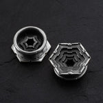 Two HEXA Futuristic Geometry Hexagon Flesh Tunnels in Silver by Kaya Movement, featuring intricate, layered designs and a central hole, lie on a dark surface. One is flat, revealing its detailed pattern, while the other stands upright, showcasing its depth and structure.