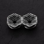 A pair of HEXA Futuristic Geometry Hexagon Flesh Tunnels in Silver by Kaya Movement is placed on a dark, textured surface. The intricate labyrinth-like design features multiple concentric layers forming a central hole in each piece, giving them a geometric and modern appearance. Available in sizes ranging from 12mm to 24mm, these earrings truly stand out.