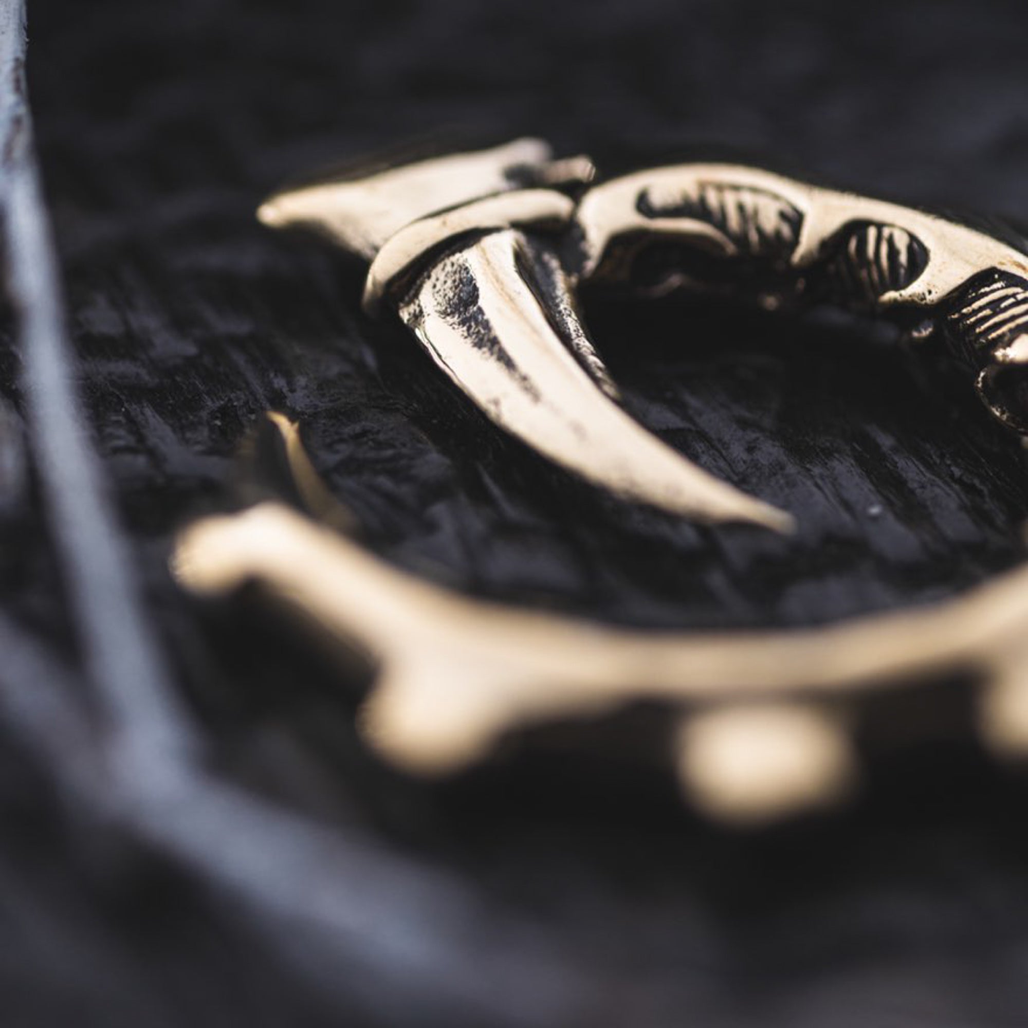 A close-up photo of the GIGER Biomechanical Open Ended Hoop Ear Weights in Gold by Kaya Movement, showcasing intricate, metallic details on a textured dark surface. The partially blurred ear weights emphasize their sharp, curved design and craftsmanship, reminiscent of accessories worn at dystopian festivals.
