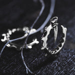 The GIGER Biomechanical Open Ended Hoop Ear Weights in Silver 925 by Kaya Movement are showcased on a dark, textured surface. Thin, string-like elements partially surround the ear weights, adding to their dramatic and edgy aesthetic reminiscent of post-apocalyptic body jewelry. The ear weights feature intricate, jagged details, evoking a sense of rugged elegance.