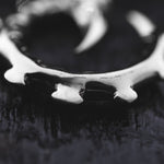 Close-up image of the GIGER Biomechanical Open Ended Hoop Ear Weights in Silver 925 by Kaya Movement, resembling post-apocalyptic body jewelry akin to a toothed ring or bear trap, placed on a textured dark surface. The focus is on the middle section of the ear weights, leaving the edges slightly blurred.