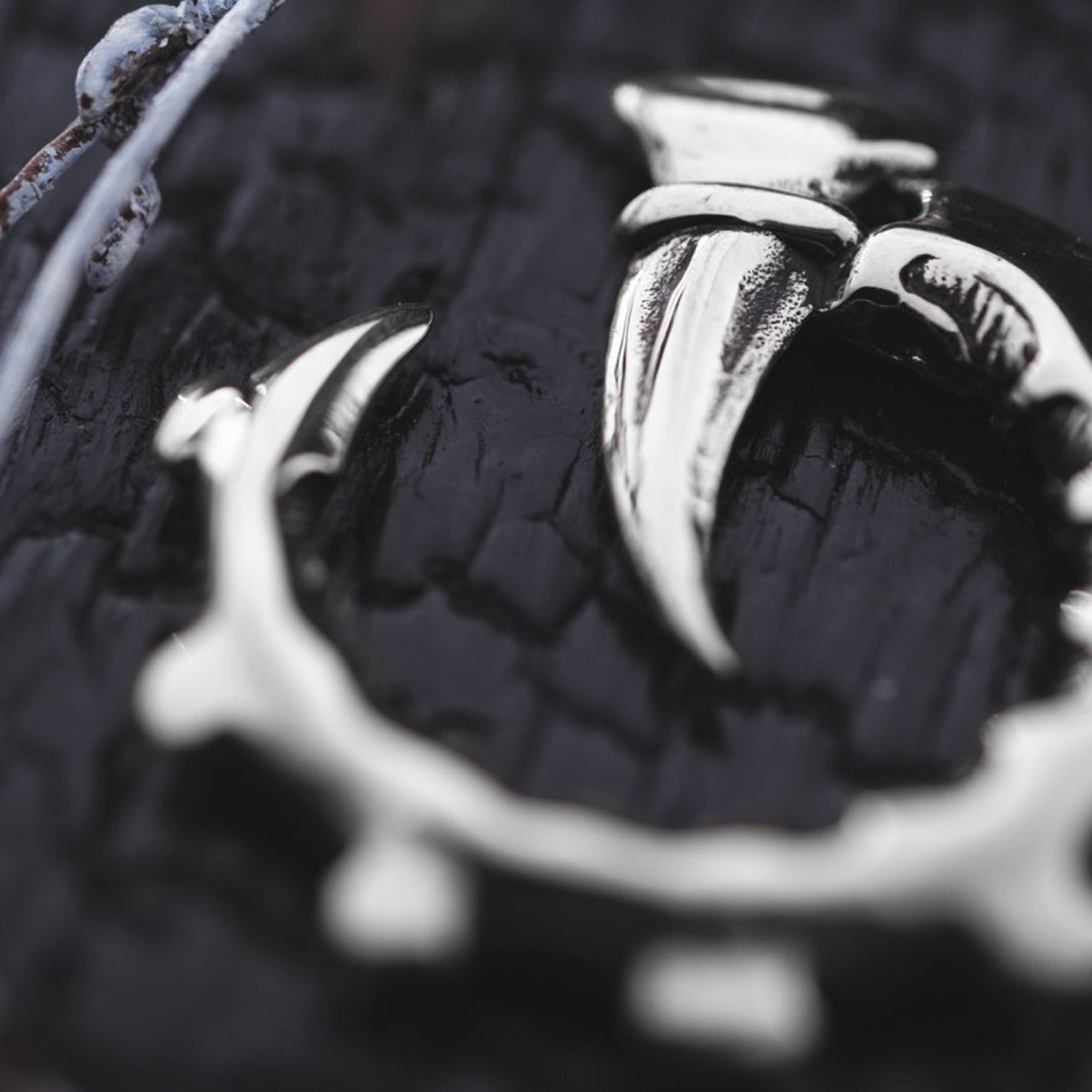 Close-up shot of a dark background highlighting the GIGER Biomechanical Open Ended Hoop Ear Weights by Kaya Movement, crafted in Silver 925. The ear weights feature sharp, talon-like protrusions and give off a post-apocalyptic vibe, with their shiny, polished surface reflecting light.