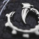 Close-up shot of a dark background highlighting the GIGER Biomechanical Open Ended Hoop Ear Weights by Kaya Movement, crafted in Silver 925. The ear weights feature sharp, talon-like protrusions and give off a post-apocalyptic vibe, with their shiny, polished surface reflecting light.