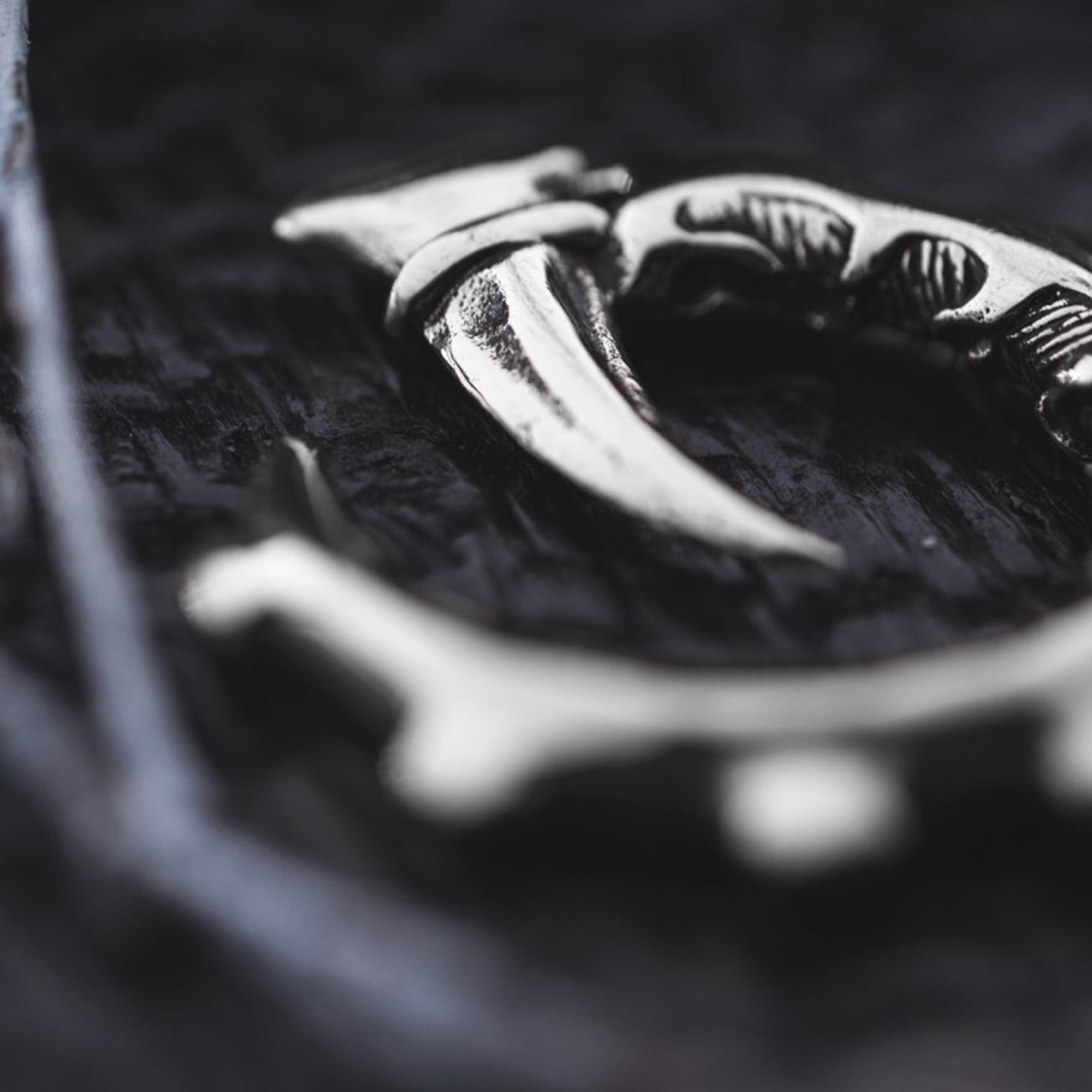 Close-up image of the GIGER Biomechanical Open Ended Hoop Ear Weights in Silver 925 by Kaya Movement, intricately designed and resting on a textured, dark surface. The 0 gauge sterling silver ear weights feature curved and pointed elements and appear polished, subtly reflecting light.