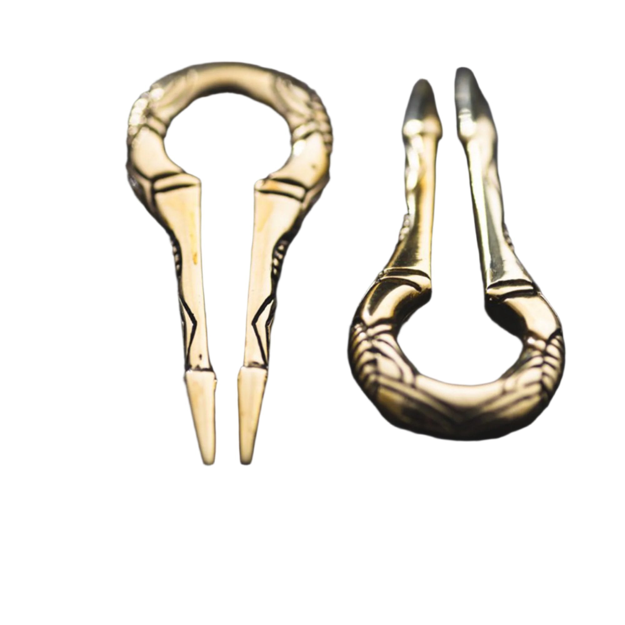 Close-up of two EXRO Biomechanical Cyborg Keyhole Ear Weights in Gold Brass by Kaya Movement against a dark, textured surface. Each piece showcases unique, detailed patterns and elaborate crafting, reminiscent of post-apocalyptic body jewelry. The lighting highlights the metallic shine and craftsmanship, enhancing their ornamental appearance.