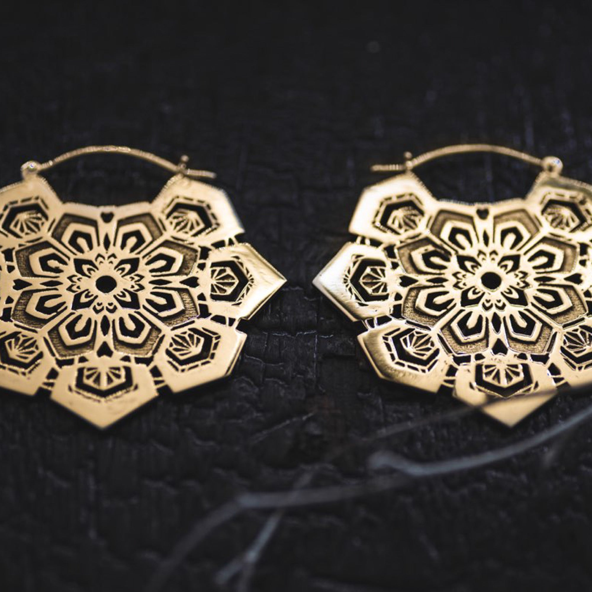 The ASA Oversized Asa No Ha Mandala Disc Earrings in Gold from Kaya Movement are intricately designed and displayed on a dark, textured background. These 16-gauge ethnic statement earrings showcase a geometric and floral-inspired pattern with delicate cutouts, creating a lacy, mandala-like appearance.