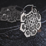 Close-up of ASA Oversized Asa No Ha Mandala Disc Earrings in Silver by Kaya Movement, featuring a detailed floral and geometric pattern reminiscent of the Asanoha motif. The earrings are placed on a dark, textured surface, emphasizing their shine and craftsmanship.