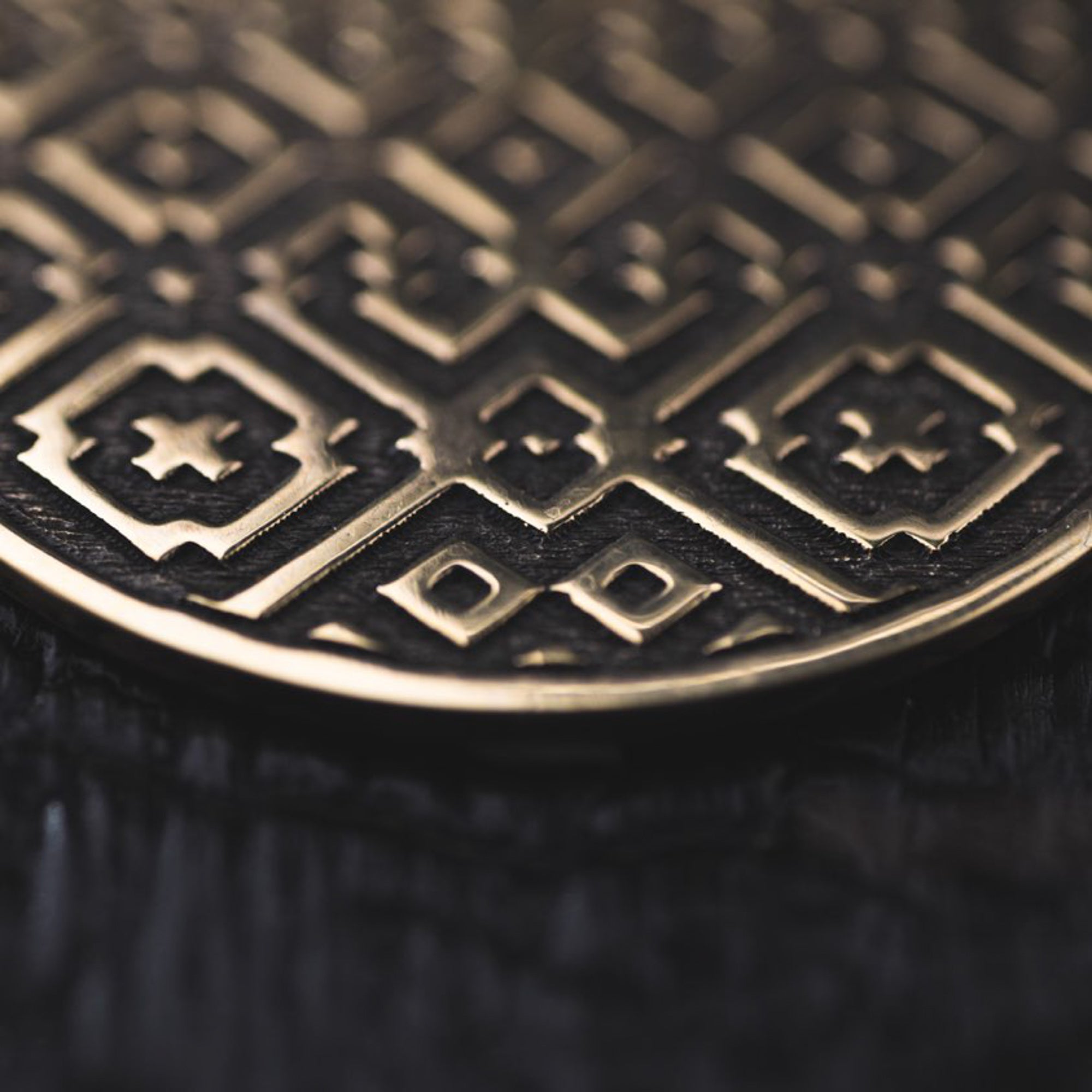 Close-up of the AREVALO Shipibo Oversized Disc Hoop Earrings in Gold by Kaya Movement, featuring intricate geometric and star patterns on their metallic surface reminiscent of Sacred geometry Shipibo designs. The detailed interlocking shapes and fine lines create a textured appearance against a dark, blurred background.