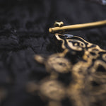 Close-up of the intricate, ornate Mozika Oversized Gothic Disc Earrings in Gold Brass by Kaya Movement, featuring detailed patterns. The focus is on a small section of these 16 gauge earrings against a dark, textured background. The craftsmanship of the design is highlighted.