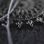 Close-up of the intricate black and silver metallic pattern on the MOZAIKA Oversized Gothic Disc Earrings in Silver by Kaya Movement, showcasing detailed filigree work reminiscent of classic Gothic designs. Thin silver threads are draped across the foreground, slightly out of focus. The dark background enhances the contrast and details, making it a striking visual.