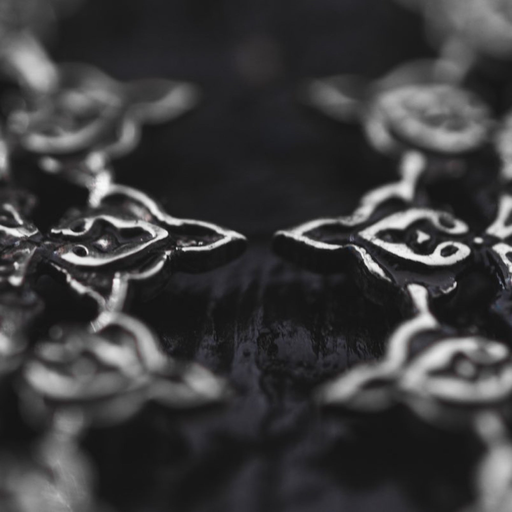 A close-up image of the MOZAIKA Oversized Gothic Disc Earrings in Silver (16 gauge) by Kaya Movement, showcasing intricately detailed metallic patterns with interconnected shapes that resemble stylized flowers or leaves. The dark and glossy background enhances the reflective quality of these exquisitely designed earrings, evoking a sense of gothic elegance.