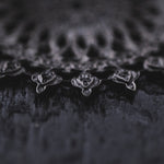 A close-up image presents the intricate design of the MOZAIKA Oversized Gothic Disc Earrings in Black by Kaya Movement. The delicate lace-like pattern against a subtly blurred black textured background highlights the 16 gauge earrings' fine details and symmetrical shapes, evoking a sense of depth and complexity. The overall tone is moody and artistic, capturing the essence of these striking accessories.