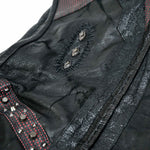 Close-up of the VENOM Men's Leather Hooded Vest Jacket from Kaya Movement, showcasing its intricate details. This black leather vest features a punk rock biker jacket design with metallic studs, red stitching, vertical textured panels, and a central patch adorned with eyelet-like embellishments surrounded by decorative stitching.