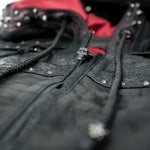 Close-up of the Kaya Movement VENOM Men's Leather Hooded Vest Jacket with intricate details. This punk rock biker jacket features studded accents and a zip with a skull-shaped pull. The inside lining is red, and it includes braided leather drawstrings.