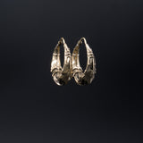 Presenting the PROMETHEUS Medium Biomechanical Hoop Earrings in Gold by Kaya Movement: these unisex earrings feature an intricate, gold-colored design with detailed, curved and woven elements that evoke biomechanical artistry. The 18 gauge hoops are set against a plain black background and have a clasp at the top for secure fastening.