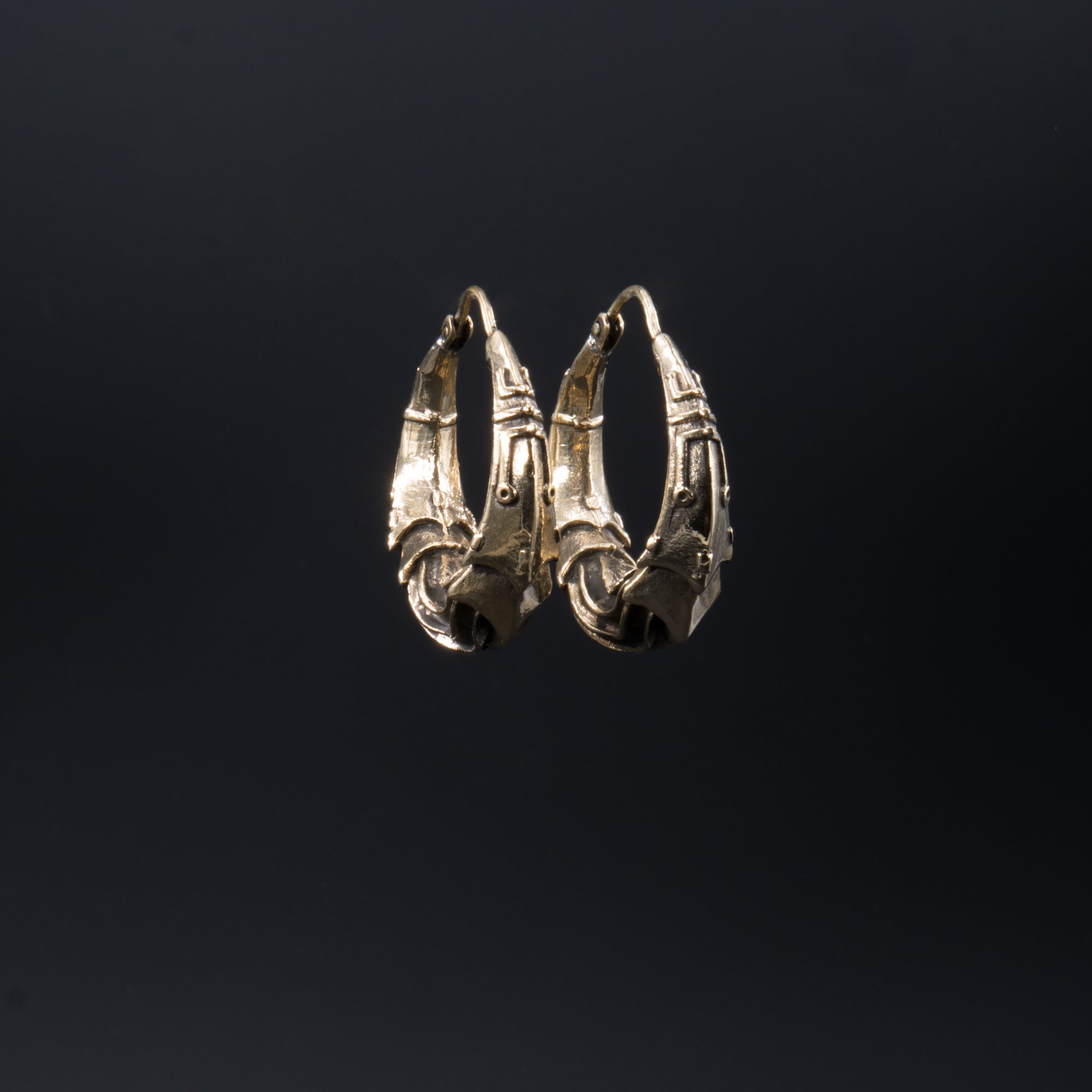 Presenting the PROMETHEUS Medium Biomechanical Hoop Earrings in Gold by Kaya Movement: these unisex earrings feature an intricate, gold-colored design with detailed, curved and woven elements that evoke biomechanical artistry. The 18 gauge hoops are set against a plain black background and have a clasp at the top for secure fastening.
