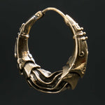 Close-up of a single PROMETHEUS Medium Biomechanical Hoop Earring in Gold by Kaya Movement, showcasing an intricate design. The 18-gauge earring features a complex and textured pattern with smooth and angular elements, creating a sculptural appearance that contrasts sharply against a dark background.