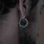 Close-up of a person's ear adorned with two 925 silver earrings: a smaller, textured hoop on the upper part of the ear and a larger, ornate hoop resembling mechanical parts on the lower lobe. The background is neutral and out of focus, highlighting these Kaya Movement PROMETHEUS Small Cyborg Hoop Earrings 18 gauge sci-fi statement earrings.