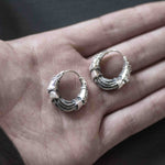 A close-up of a person's open hand holding the PROMETHEUS Small Cyborg Hoop Earrings by Kaya Movement. Crafted from 925 silver and featuring an intricate design of interlocking segments, these sci-fi statement earrings boast a bold and stylish appearance.