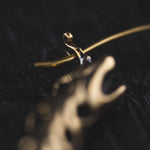 Close-up of the QUETZALCOATL Oversized Snake Spine Hoop Earrings in Gold by Kaya Movement. The earrings appear shiny and are artistically designed with blurred details. The background is dark, causing the gold to stand out prominently, much like delicate gold chains would in a sophisticated setting. The image has a shallow depth of field, focusing mainly on the intricate detailing of the hoops.