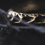 A close-up image of intricately detailed, gold-colored QUETZALCOATL Oversized Snake Spine Hoop Earrings in Gold by Kaya Movement on a dark surface. The focus is on the textured design of the earrings, which includes swirling patterns reminiscent of post-apocalyptic body jewelry. The background is blurred, emphasizing the earrings' craftsmanship and metallic sheen.