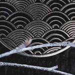 Close-up of the SEIGAIHA Oversized Japanese Geometry Disc Earrings in Silver by Kaya Movement, featuring an intricate pattern of overlapping semicircles reminiscent of waves, set against a dark background. A frosted branch is partially covering the earrings in the foreground, enhancing their boho statement appeal.
