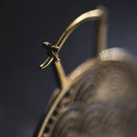 Close-up of the SEIGAIHA Oversized Japanese Geometry Disc Earrings in Gold by Kaya Movement, showcasing the intricate patterns reminiscent of tribal jewelry. The focus is on a small figure perched at the center, holding a bow-like structure. The blurred background emphasizes the delicate details of this unisex statement piece, made with 16 gauge gold.
