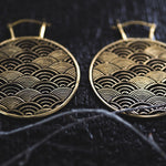 Close-up image of a pair of SEIGAIHA Oversized Japanese Geometry Disc Earrings in Gold by Kaya Movement, featuring an intricate overlapping fan pattern. The dark background accentuates the fine details and craftsmanship of these 16-gauge unisex statement earrings.