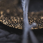 A close-up image showcasing the intricate gold detailing of the OLIVIA Tribal Shipibo Seamless Disc Hoop Earrings in Gold from Kaya Movement. The foreground is intentionally blurred, creating an abstract, artistic feel while emphasizing the rich patterns and textures of these 12 gauge tribal-inspired earrings in the background.