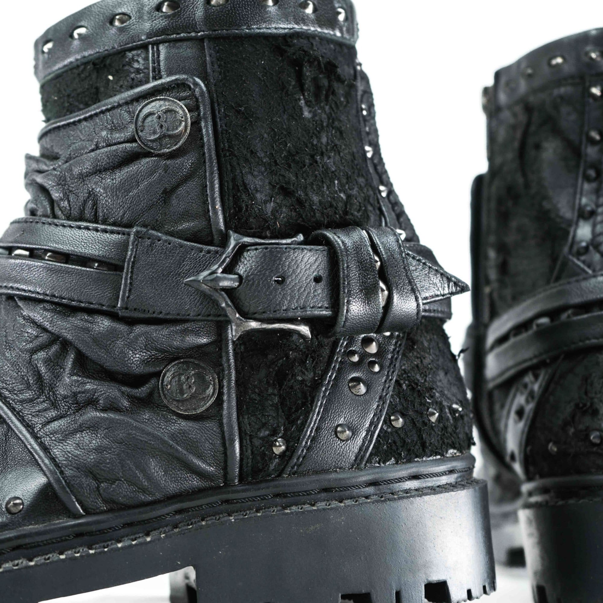 Close-up of stylish MAGMA Wasteland Studded Leather Ankle Combat Boots by Kaya Movement, featuring buckle straps and metal studs that showcase their intricate texture and rugged design. These boots have a thick sole and detailed stitching, adding to their edgy and contemporary look.