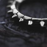 A close-up photo captures the KALASH Medium Spike Hoop Clicker Ear Weights in Silver Brass by Kaya Movement, showcasing its sharp, pointed spikes evenly spaced around the circumference. Resembling tribal punk industrial jewelry, the 4 gauge ring rests on a dark, textured surface, creating a striking contrast between the polished metal and the background.