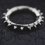 A close-up shot of the KALASH Medium Spike Hoop Clicker Ear Weights in Silver Brass by Kaya Movement, featuring small, evenly spaced spikes around their circumference, resting on a dark, textured surface. Reminiscent of tribal punk industrial jewelry, the ear weights have a polished finish and the spikes add a bold, edgy aesthetic to their design.