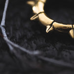 Close-up image of the KALASH Small Spike Hoop Clicker Ear Weights in Gold Brass (4 gauge), by Kaya Movement, partially visible on a dark, textured surface with a thin, white branch nearby. The spikes of the ear weights and the rough background create a stark contrast, highlighting their shiny and detailed design, reminiscent of post-apocalyptic body jewelry.