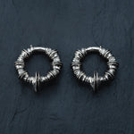 Introducing the TRAKARA Heavy Tribal Cyborg Clicker Ear Weights in Silver by Kaya Movement, intricately designed with multiple small segments and pointed studs in a circular pattern, reminiscent of tribal cyborg aesthetics against a dark textured backdrop.