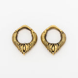 A pair of MARVDASHT Small Cyborg Hoop Clicker Ear Weights in Gold from Kaya Movement on a white background, featuring intricate teardrop designs with detailed carvings. Each earring showcases a central motif resembling an eye, making them perfect for fans of post-apocalyptic body jewelry.