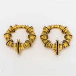 A pair of gold TRAKARA Heavy Tribal Cyborg Clicker Ear Weights from Kaya Movement, featuring a 2 gauge size. The ear weights showcase an intricate, round design with elaborate segmented patterns and textured detailing, creating a decorative and elegant appearance reminiscent of tribal cyborg aesthetics. Each piece includes a pointed, symmetrical decoration at the center.