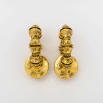 A pair of TRAKARA Heavy Tribal Cyborg Clicker Ear Weights in Gold by Kaya Movement, featuring a round base with ornate floral patterns, sit against a plain white background. These 2 gauge earrings have a traditional, antique look that seamlessly blends history with futuristic elements.