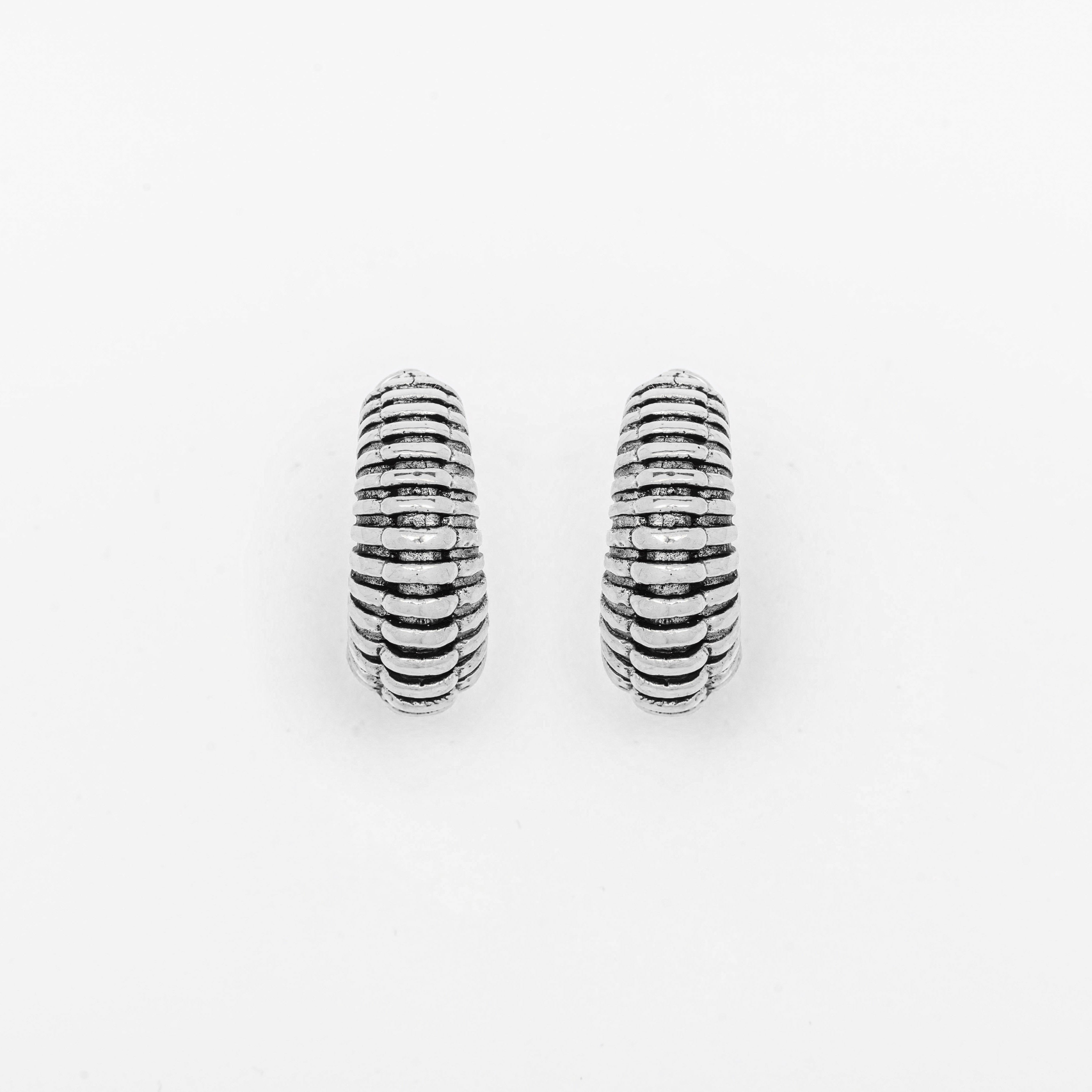 A pair of TRILOBITE Small Biomechanical Clicker Ear Weights in Silver Brass (2 gauge) by Kaya Movement, showcased against a white background. The ear weights feature parallel grooves encircling them, contributing to a textured appearance reminiscent of biomechanical cyborg earrings.