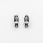 A pair of TRILOBITE Small Biomechanical Clicker Ear Weights in Silver Brass (2 gauge) by Kaya Movement, showcased against a white background. The ear weights feature parallel grooves encircling them, contributing to a textured appearance reminiscent of biomechanical cyborg earrings.