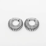 A pair of TRILOBITE Small Biomechanical Clicker Ear Weights in Silver Brass from Kaya Movement is displayed against a plain white background. The 2 gauge ear weights are positioned side by side, showcasing their ribbed, textured design with detailed grooves and a reflective surface reminiscent of futuristic stretched ear jewelry.