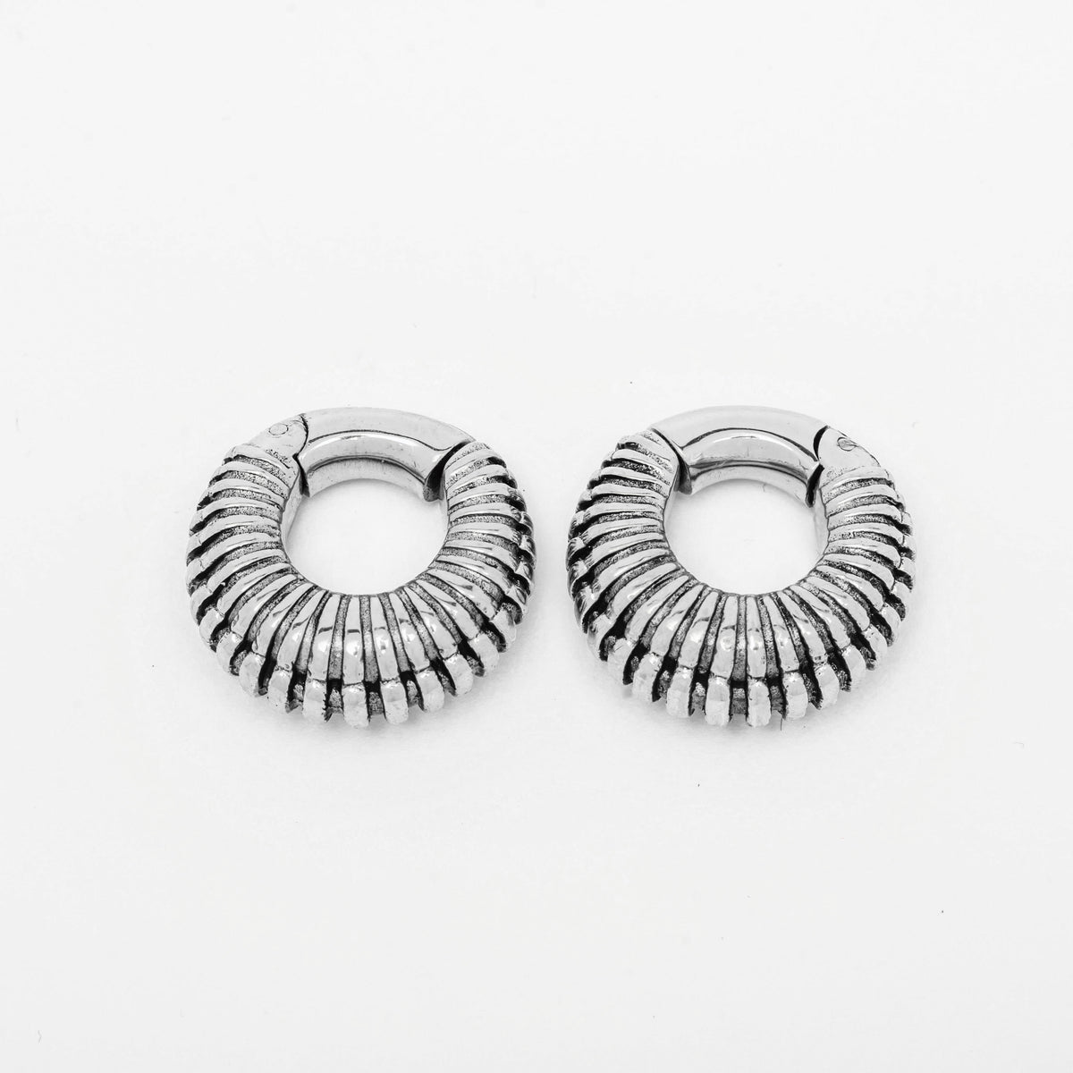 A pair of TRILOBITE Small Biomechanical Clicker Ear Weights in Silver Brass from Kaya Movement is displayed against a plain white background. The 2 gauge ear weights are positioned side by side, showcasing their ribbed, textured design with detailed grooves and a reflective surface reminiscent of futuristic stretched ear jewelry.
