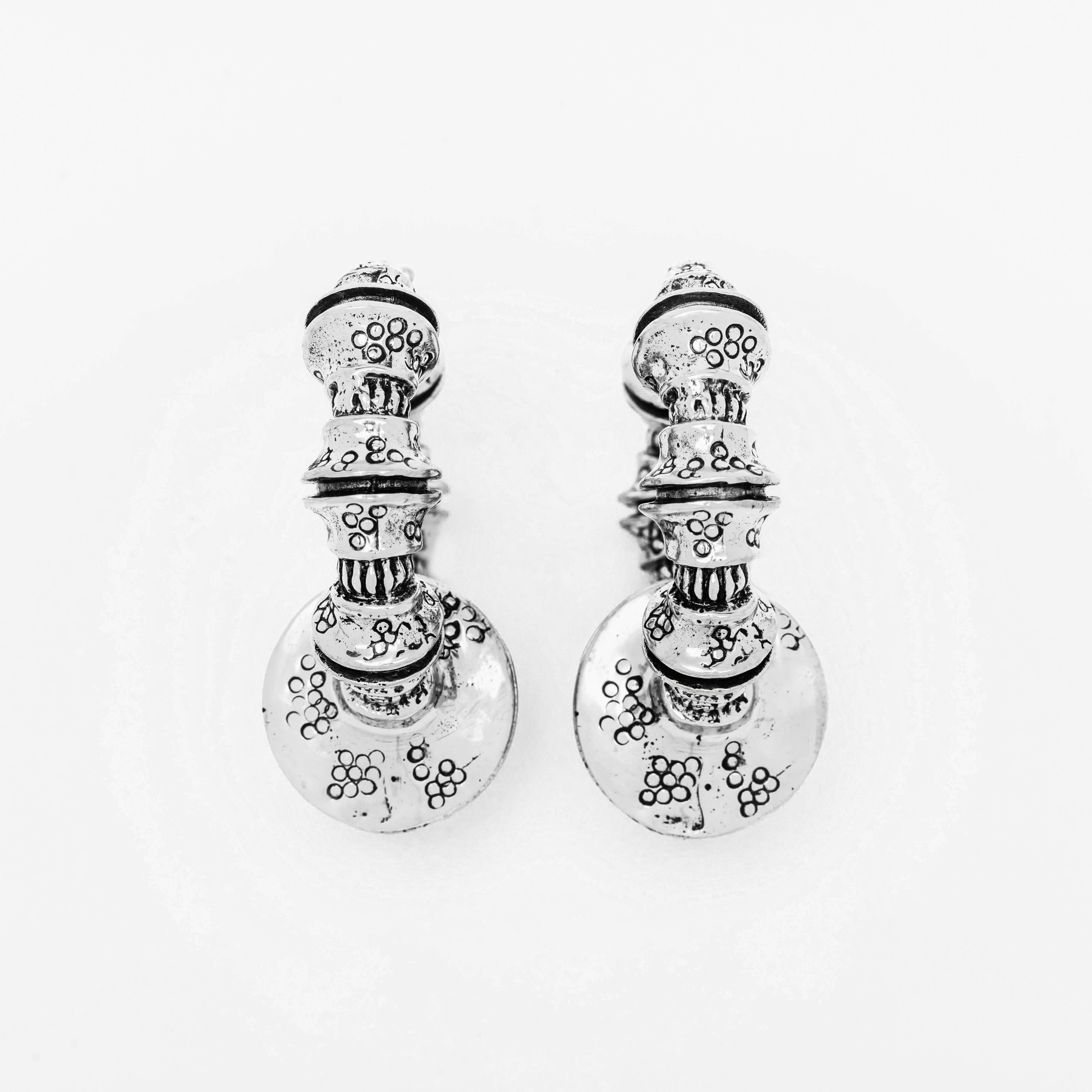 A pair of Kaya Movement's TRAKARA Heavy Tribal Cyborg Clicker Ear Weights in Silver, designed for 2 gauge ears, featuring intricate engraved floral patterns. These earrings boast multiple stacked circular elements with detailed designs and a larger disc at the bottom, all inspired by traditional or vintage aesthetics.