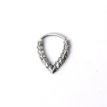 The KAMO Biomech Teardrop Clicker Septum Ring in silver, crafted by Kaya Movement, features a V-shaped design adorned with a series of small, square-like beads along the inner side that create a patterned and textured appearance. This 16-gauge piece of handcrafted body jewelry is displayed against a plain white background.