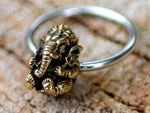 Introducing the GANESHA Silver Ring with Gold Pendant by Kaya Movement, a beautifully handcrafted piece showcasing a detailed brass figurine of Ganesha, the revered Hindu deity with an elephant head. The ring is elegantly set against a textured, natural background. Available in 18, 16, or 14 gauge.