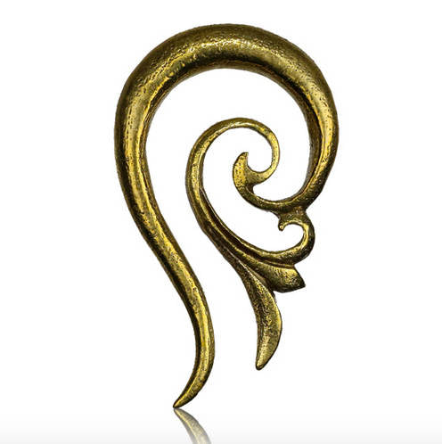 The TILA Spiral Ear Hangers in Gold by Kaya Movement feature an ornate, elongated design resembling a stylized ear, characterized by intricate flowing curves and a shiny metallic finish. Crafted from yellow brass, their smooth, reflective surface exudes the essence of feminine elegance, all set against a plain white background.