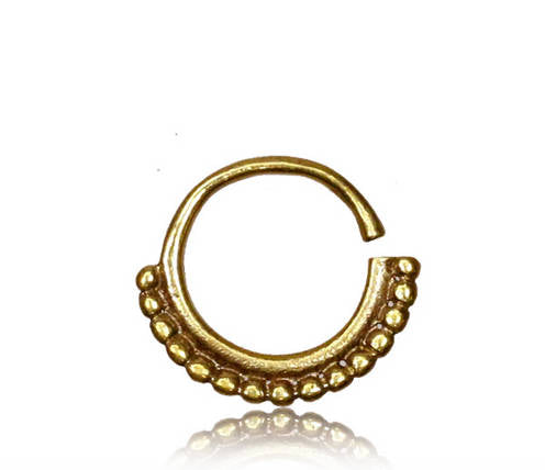 The IRI Seamless Septum Ring in Gold by Kaya Movement is a small, circular nose ring crafted with a textured design on the bottom half that features a series of small gold beads. This 16 gauge, shiny metal piece is open on one side and reflects light beautifully against a white background, highlighting its intricate craftsmanship and subtle tribal ethnic design.