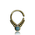 A decorative gold septum ring with an open design, featuring a beautiful opal at its center. The ring has small gold beads on either side of the stone, arranged symmetrically in a triangle shape. The reflective surface underneath creates a faint mirror image of the ring, reminiscent of elegant 18g jewelry from Kaya Movement's Unique Gold Triangle Septum Ring collection. This piece exudes a cute witchy goddess vibe with its oxidized gothic aesthetic.