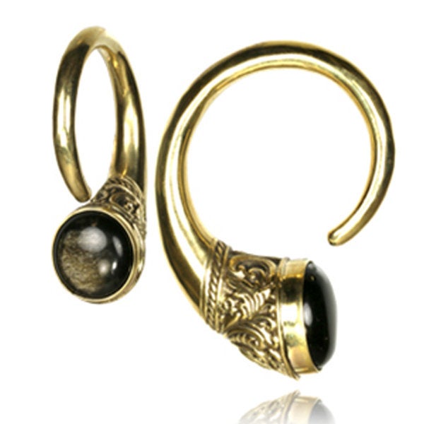 The IRO Dangle Ear Weights in Gold & Golden Obsidian 6mm (2 gauge) by Kaya Movement feature an intricate gold spiral design with detailed engravings and accents of black golden obsidian gemstones. Each ear weight showcases a round black stone set within an ornate, carved gold frame. This elegant brass jewelry combines traditional craftsmanship with a tribal feel and a modern twist.