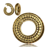 The Kaya Movement SILO Seamless Hoop Ear Weights in Gold with Clicker, featuring a large circular pendant and matching earrings, showcase an antique and intricate design. Both pieces have a pattern of raised circular dots arranged concentrically, reminiscent of tribal gold ear weights. They rest against a plain white background, highlighting their geometric elegance.