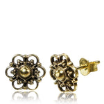 A pair of ornate ear jewelry, the MIA Flower Stud Earrings in Gold by Kaya Movement boast a floral design. Each earring features a central gold bead surrounded by intricate filigree petals, accented with small dots. One earring lies flat while the other stands to display the post and butterfly backing, all housed in elegant packaging.